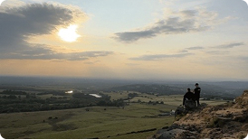 Person sitting on a hill overlooking a sunset landscape